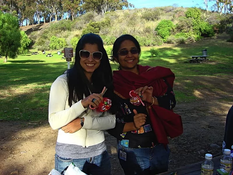 Two lab members are leaning into each other, smiling during a day at the park. They are holding candy canes. Picnic tables are in the background.