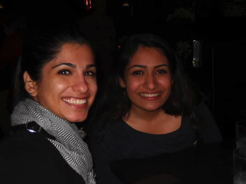 Two students are seated in a dimly lit restaurant, looking directly at the camera and smiling.