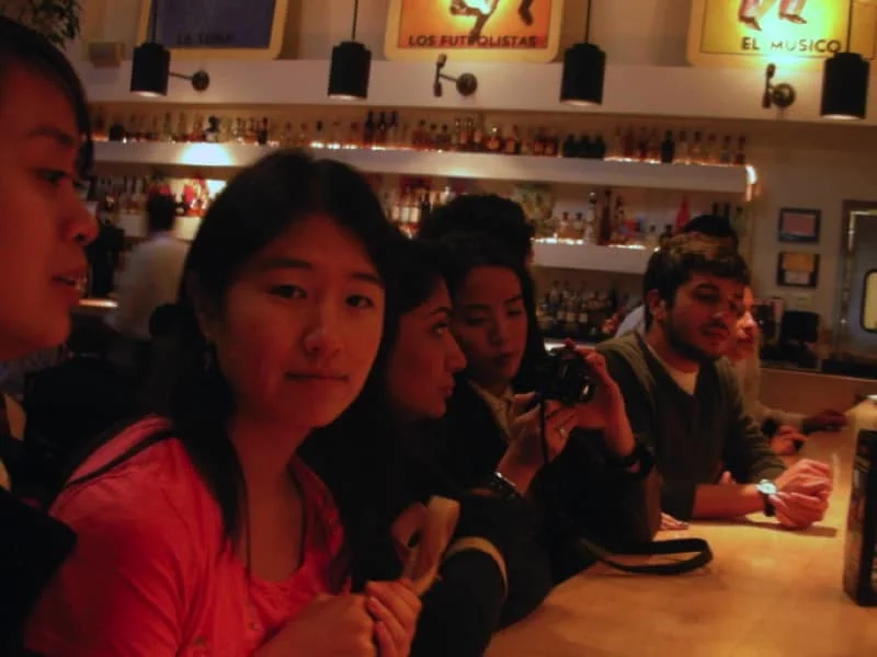 Bitan Lab members sit at a long wooden table for dinner. They're talking and showing each other their phones.
