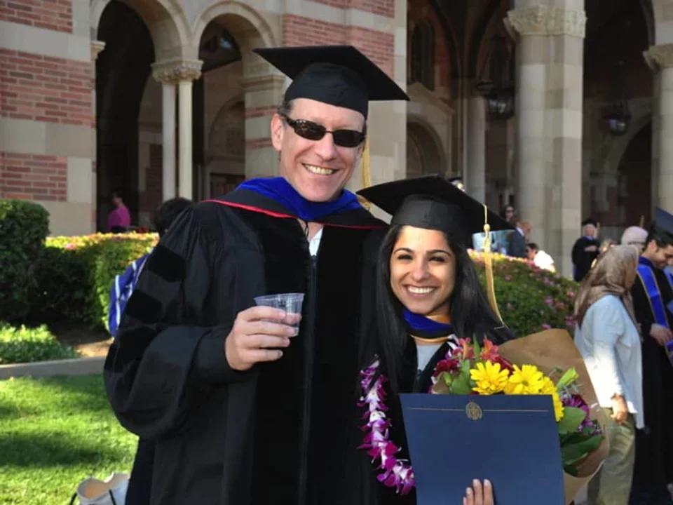 Dr. Bitan and one of his researchers are wearing graduation caps and gowns. They are smiling wide because his student had just earned her PhD.