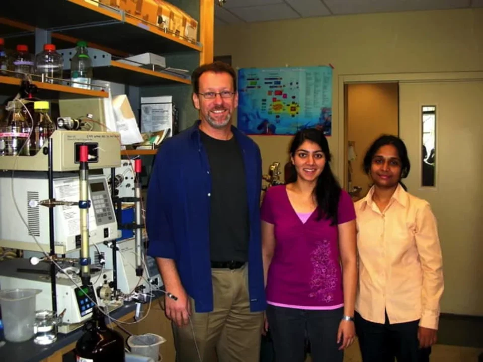Two students stand next to Dr. Bitan. Lab equipment is to their left.