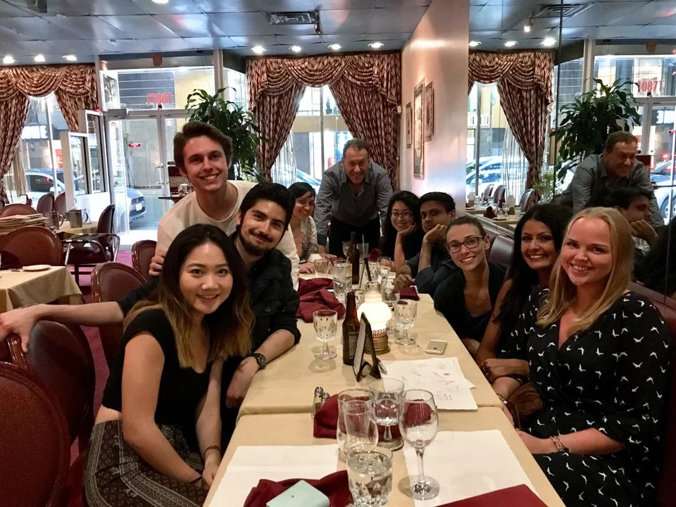 Nine students sit down a long rectangular table. Dr. Bitan is standing at the end of the table. Everyone is looking at the camera, smiling.