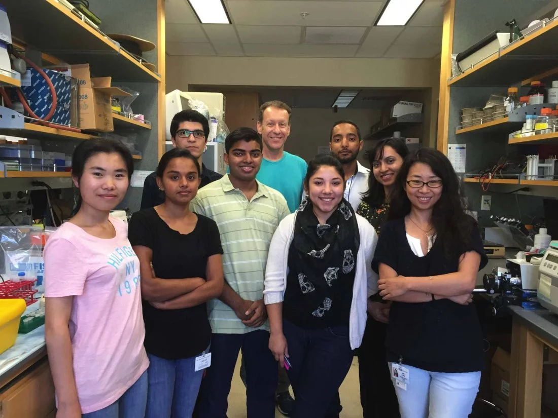 A group of Bitan Lab researchers stand in the middle of the lab with Dr. Bitan.