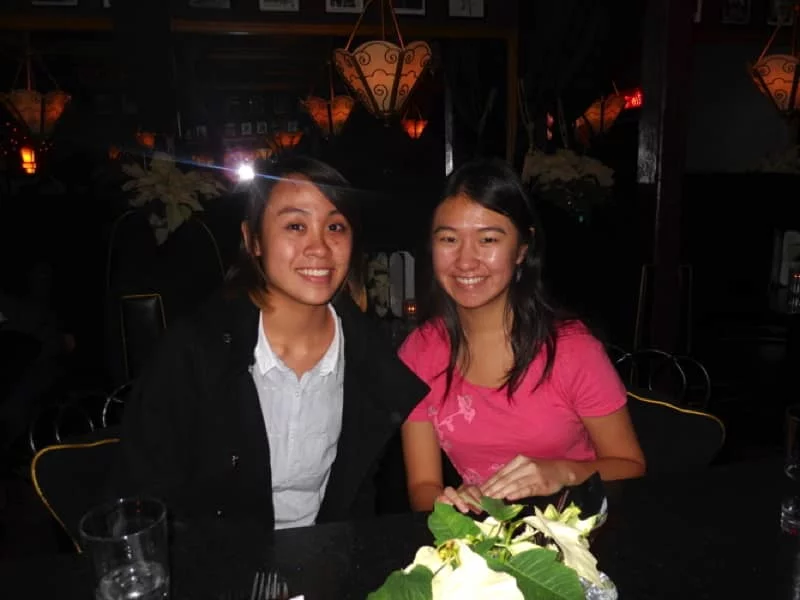 Two students are seated and smiling in a dimly lit restaurant.