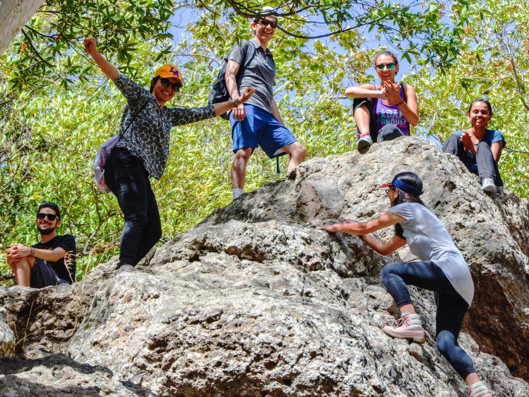 Six students enjoy the great outdoors and sit atop of a large rock during a group outing.